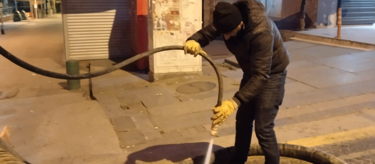 Ekip üyesi gece vardiyasında tazyikli su ile rögar temizliği yapıyor